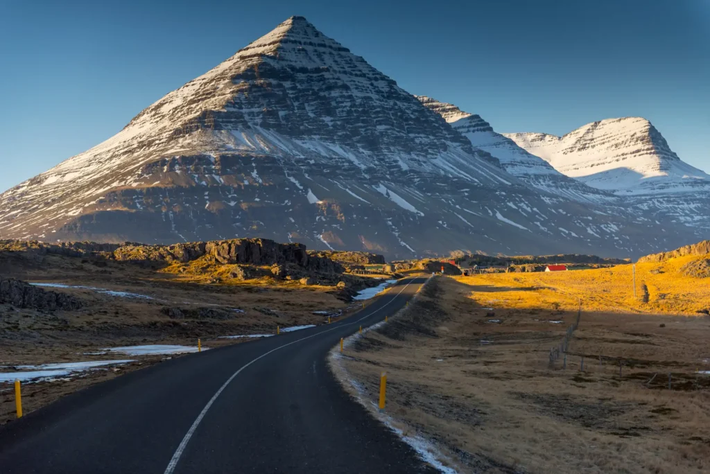 A quiet road leading towards the snow-dusted peak of Búlandstindur in East Iceland, bathed in low winter light beneath a clear sky.